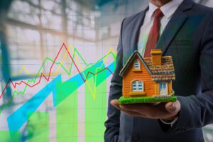 Businessman presenting model home against backdrop of rising market graphs, symbolizing growth post-interim budget announcement.