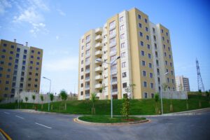 Newly constructed residential properties in Gurgaon with yellow apartment buildings, lush greenery, and a clear road under a blue sky.