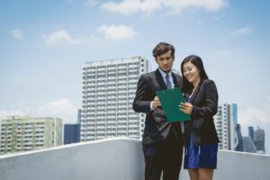 Two real estate professionals discussing service apartments in Gurgaon, reviewing documents on a rooftop with cityscape in the background.